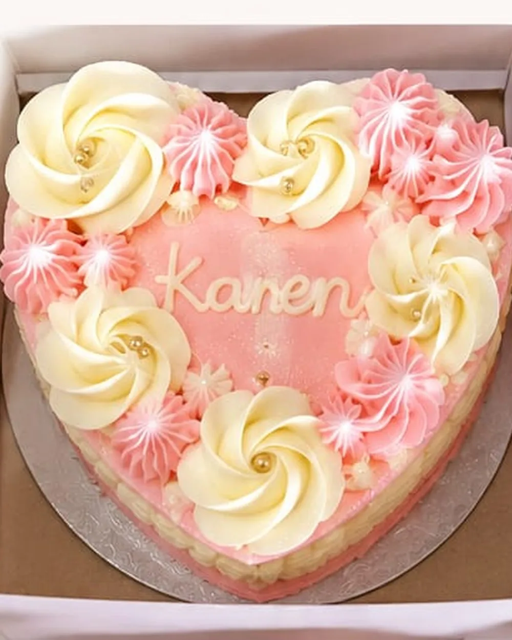 A pink and cream heart-shaped bento cake piped with buttercream rosettes, in an open cake box