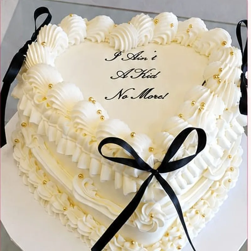 An ivory heart-shaped cake with piped ruffles, gold pearls and a black satin bow