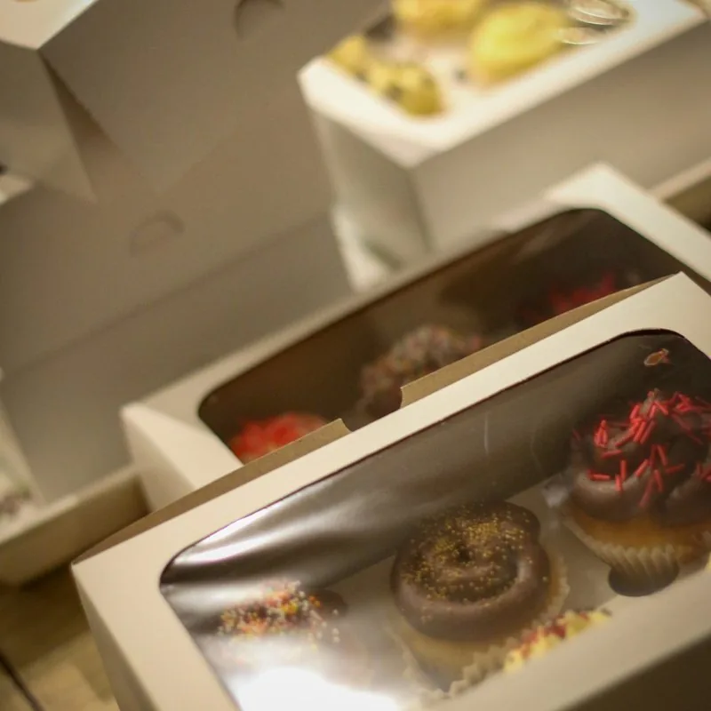 White cake boxes with clear window lids, holding decorated cupcakes