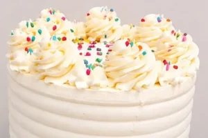 A tall cake with a smooth buttercream finish, sprinkles and piped swirls